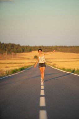 Genç bir kız, yalnız ve düz bir yolun ortasında yürüyor, günün geç saatlerinde. Elleri haç şeklinde gerilmiş, dengeyi sağlamak ve bölünme çizgisinden düşmemek için..