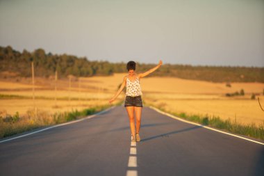 Genç bir kız, yalnız ve düz bir yolun ortasında yürüyor, günün geç saatlerinde. Elleri haç şeklinde gerilmiş, dengeyi sağlamak ve bölünme çizgisinden düşmemek için..
