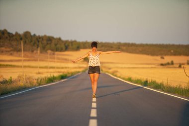 Genç bir kız, yalnız ve düz bir yolun ortasında yürüyor, günün geç saatlerinde. Elleri haç şeklinde gerilmiş, dengeyi sağlamak ve bölünme çizgisinden düşmemek için..