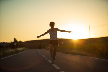 Genç bir kız, yalnız ve düz bir yolun ortasında yürüyor, günün geç saatlerinde. Elleri haç şeklinde gerilmiş, dengeyi sağlamak ve bölünme çizgisinden düşmemek için..