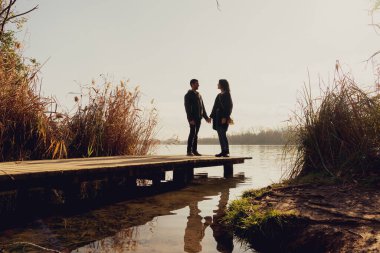 Göldeki bir limanda genç ve mutlu bir çift. Gün batımında. El ele tutuşup birbirinize bakıyorsunuz..