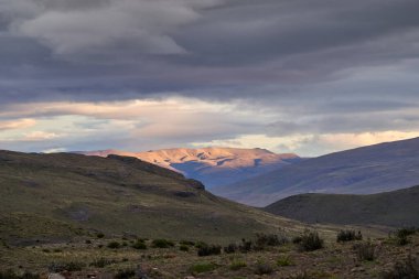 Torres del Paine Ulusal Parkı 'nın dağları üzerinde kasvetli bir günbatımı altın güneş ışığı ve gökyüzünde dramatik bulutlar, Şili Güney Amerika