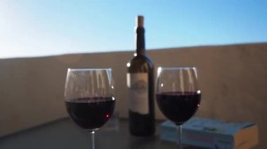 İki kadeh kırmızı şarap bulanık arka planda bir şişenin önünde duruyor.