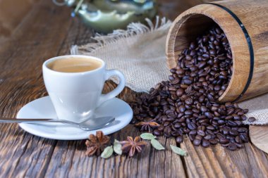 Espresso fincanı ve arka planda kavrulmuş kahve çekirdekleri eski ahşap bir masanın üstünde..