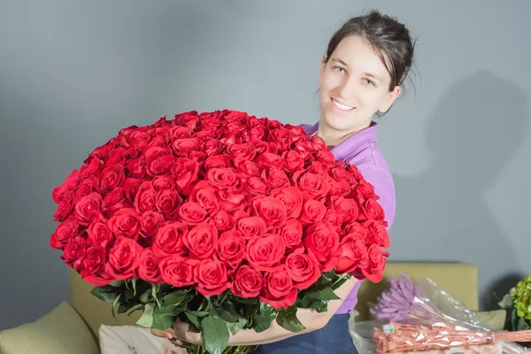 Florist woman prepares a big bouquet of red roses