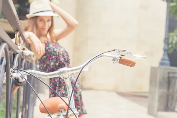 Chica joven de pie cerca de la cerca, cerca de la bicicleta de la ciudad vintage — Foto de Stock