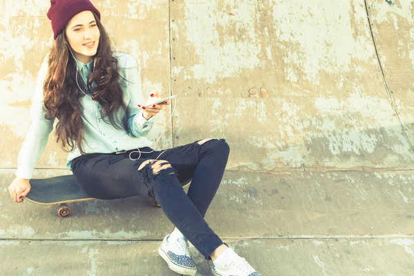 Hipster skateboarder chica con monopatín al aire libre sentado en skatepark — Foto de Stock