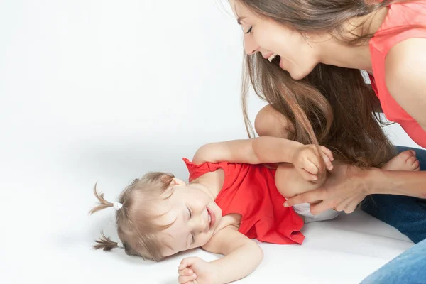 Funny baby girl lying near happy mother on white bed — Stock Photo, Image