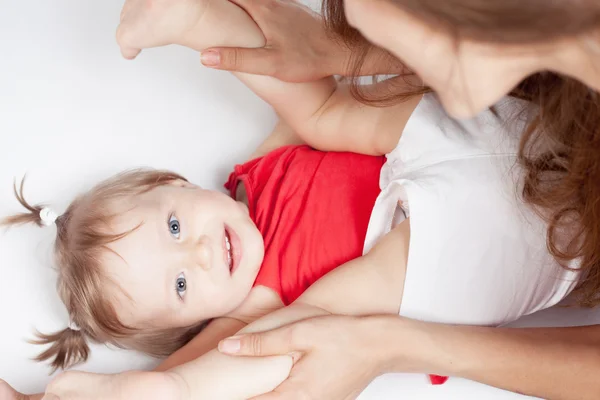 Funny baby girl lying near happy mother on white bed — Stock Photo, Image