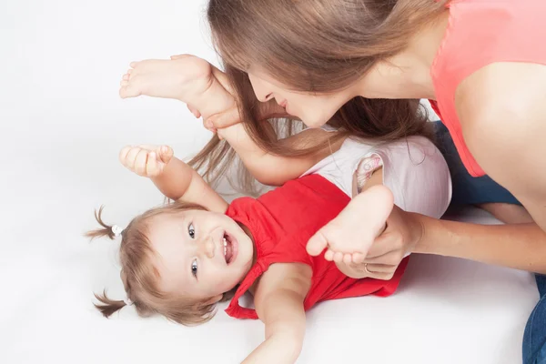 Funny baby girl lying near happy mother on white bed — Stock Photo, Image