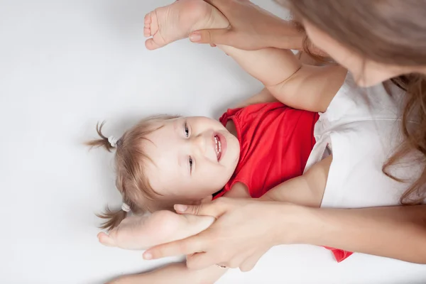 Funny baby flicka låg nära glad mamma på vit säng — Stockfoto