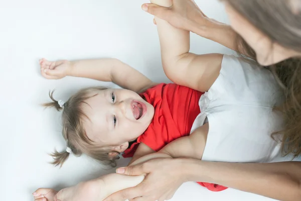 Funny baby flicka låg nära glad mamma på vit säng — Stockfoto