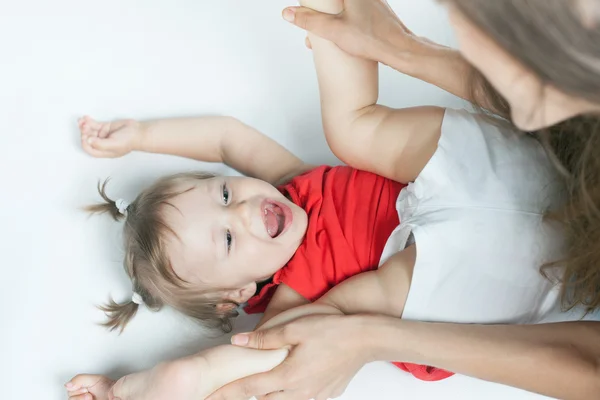 Funny baby girl lying near happy mother on white bed — Stock Photo, Image