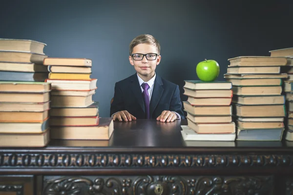 Slimme school jongen zit aan tafel met vele boeken — Stockfoto