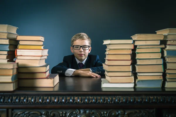 Smart skola pojke sitter vid bord med många böcker — Stockfoto