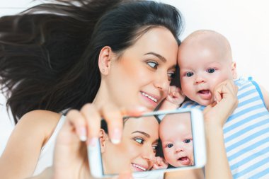 Funny baby and mother make selfie on mobile phone clipart