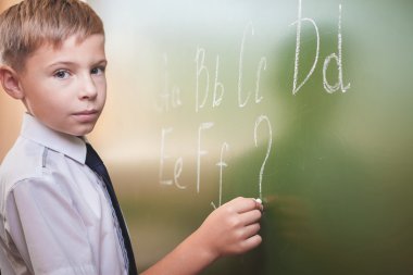 Okullu çocuk İngilizce alfabesi ile Tebeşir tahtaya yazar.