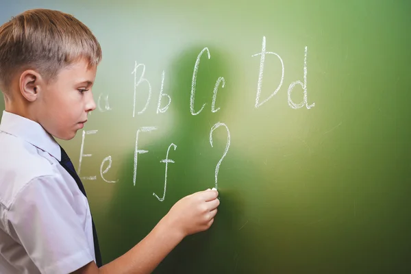 Menino da escola escreve alfabeto inglês com giz no quadro negro — Fotografia de Stock