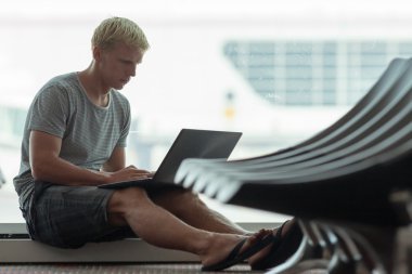 Havaalanında dizüstü bilgisayar kullanan genç adam