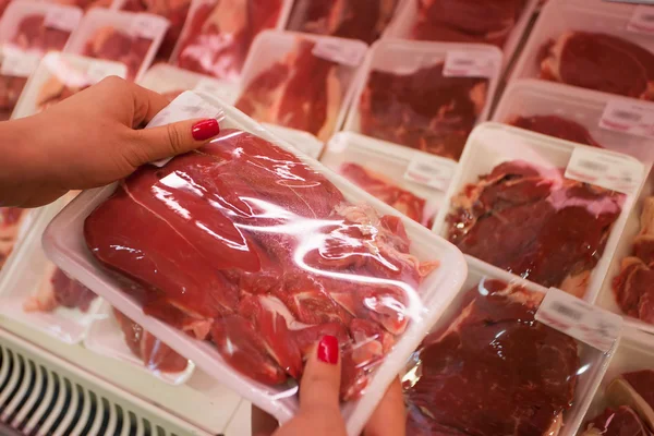 Verpacktes Fleisch mit Frauenhand im Supermarkt lizenzfreie Stockfotos