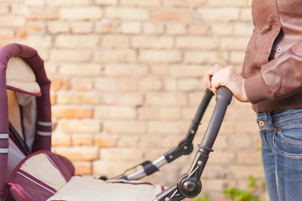 Happy mother at outdoor shakes a baby carriage — Stock Photo, Image