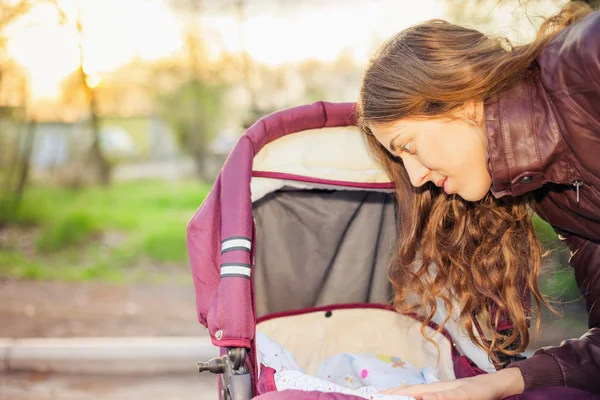 Glad mamma på utomhus skakar en barnvagn — Stockfoto