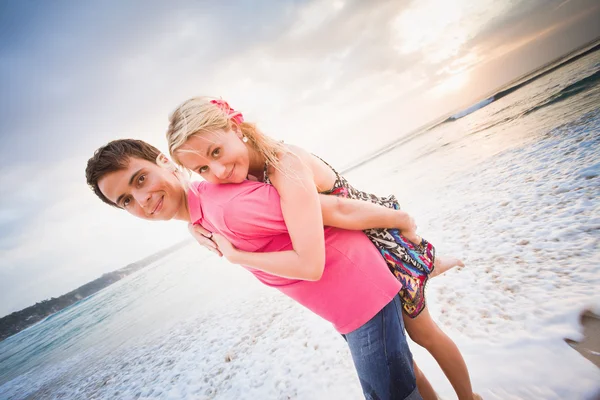 Girlfriend riding on the back of her boyfriend and happy looking at the camera — Stockfoto