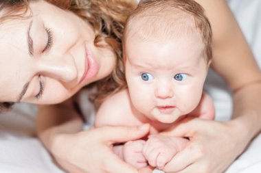Happy mother with a baby lying on a white bed