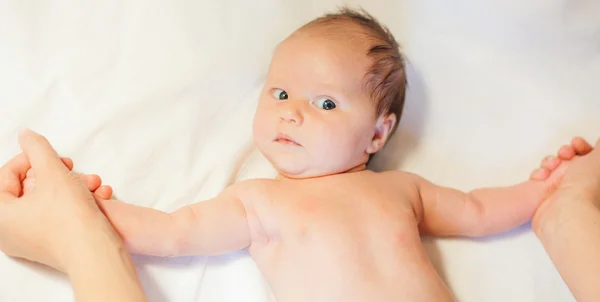 Mother makes baby stretching with happy newborn at white bed — Stock Photo, Image