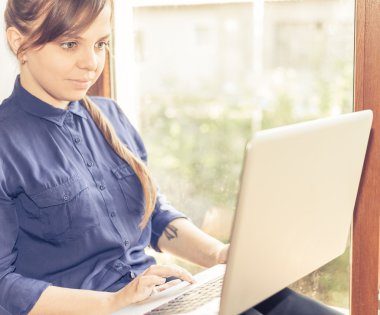 Beautiful happy student with a laptop sitting against bright window