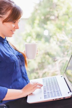 Beautiful happy student with a laptop sitting against bright window