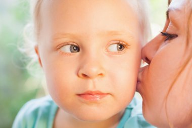 Mom kissing pretty daughter, with beautiful eyes and blonde hair