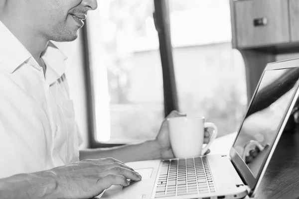 Young man uses laptop at his workplace at home against window — Stock Photo, Image