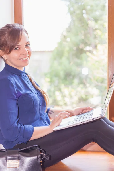 Beautiful happy student with a laptop sitting against bright window — Stock Photo, Image