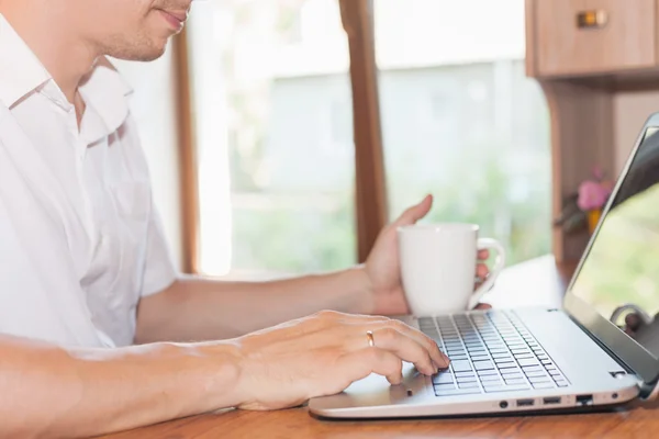 Young man uses laptop at his workplace at home against window — Stock Photo, Image