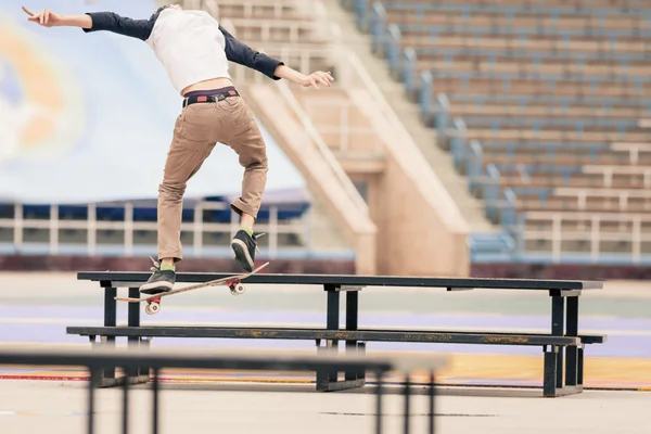 Teenager doing a trick by skateboard on a rail in skate park — Stok fotoğraf