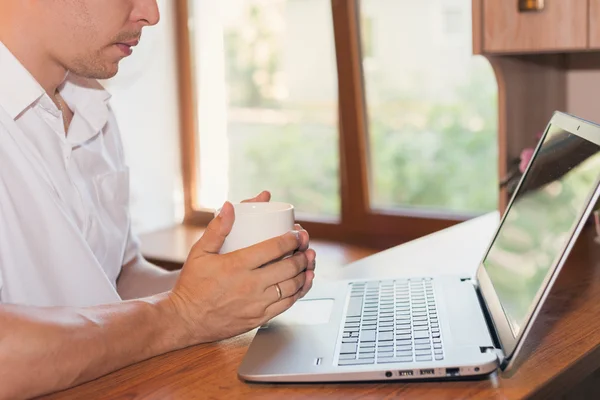 Young man uses laptop and drinking coffee or tea at his workplace — Stock Photo, Image