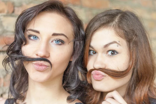 Two young pretty girls making mustache of their hair — Stock fotografie