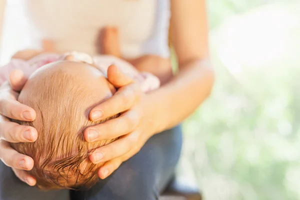 Mãe segurando a cabeça do bebê às mãos — Fotografia de Stock
