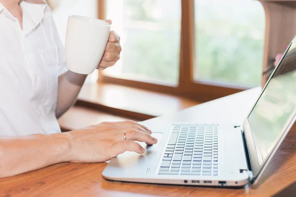 Young man uses laptop and drinking coffee or tea at his workplace — Zdjęcie stockowe