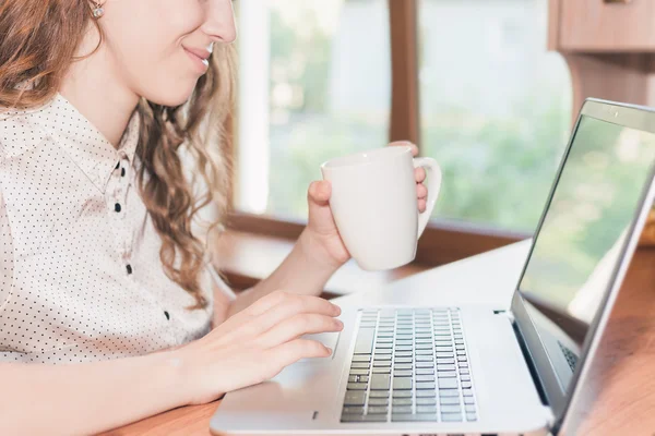 Young pretty girl working at laptop and drinking coffee — Stock Photo, Image