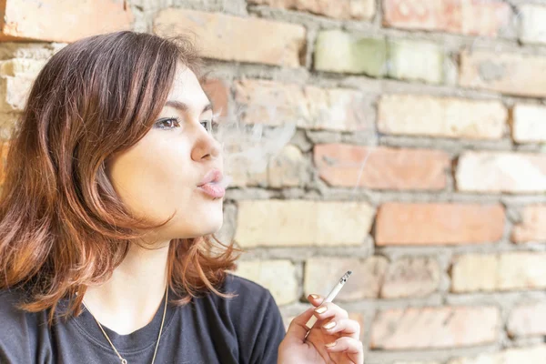 Colegiala adolescente fuma al aire libre en ladrillo fondo de la pared — Foto de Stock