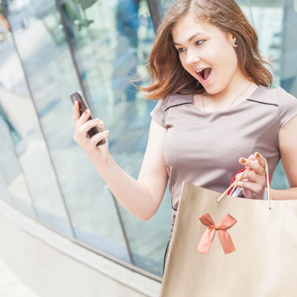 Happy fashion woman with bag using mobile phone, shopping center — Stock Photo, Image