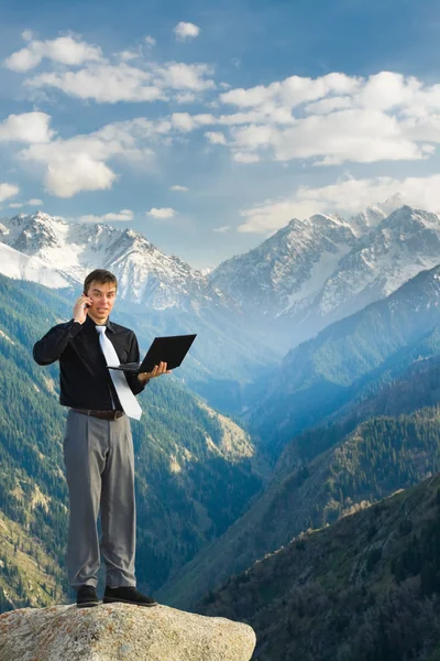 Młody biznesmen z jego laptopa rozmawiać przez telefon w górach — Zdjęcie stockowe