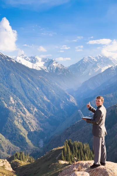 Forretningsmand med laptop på toppen af bjerget er venligst - Stock-foto