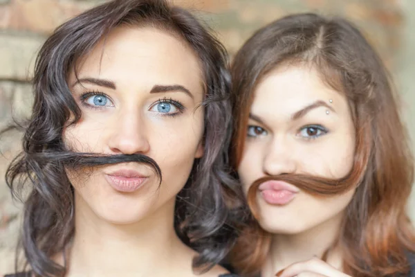 Two young pretty girls making mustache of their hair — Stock fotografie