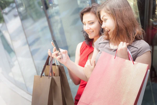 Mulheres de moda feliz com sacos usando telefone celular, centro comercial — Fotografia de Stock