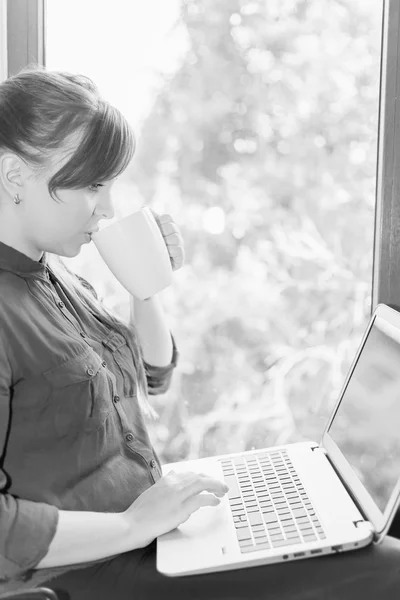 Estudante feliz bonita com um laptop sentado contra a janela — Fotografia de Stock