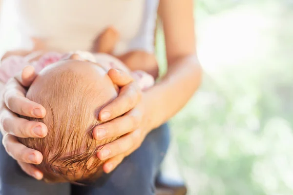 Mãe segurando a cabeça do bebê às mãos — Fotografia de Stock