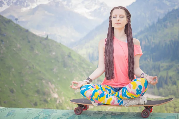 Hippie fashion girl doing yoga, relaxing on skateboard at mountain — Stock Photo, Image